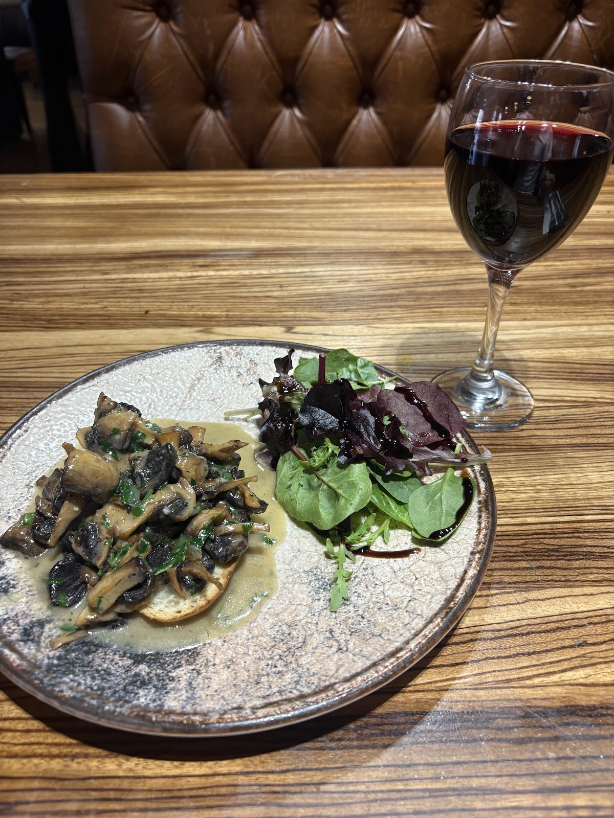 Mushroom bruschetta with dressed leaves and a glass of red wine