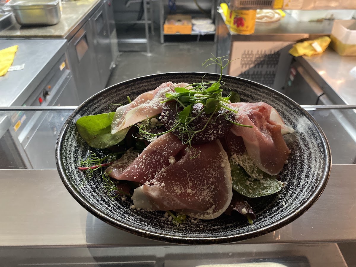 Cured ham with parmesan and pea shoots in a black bowl