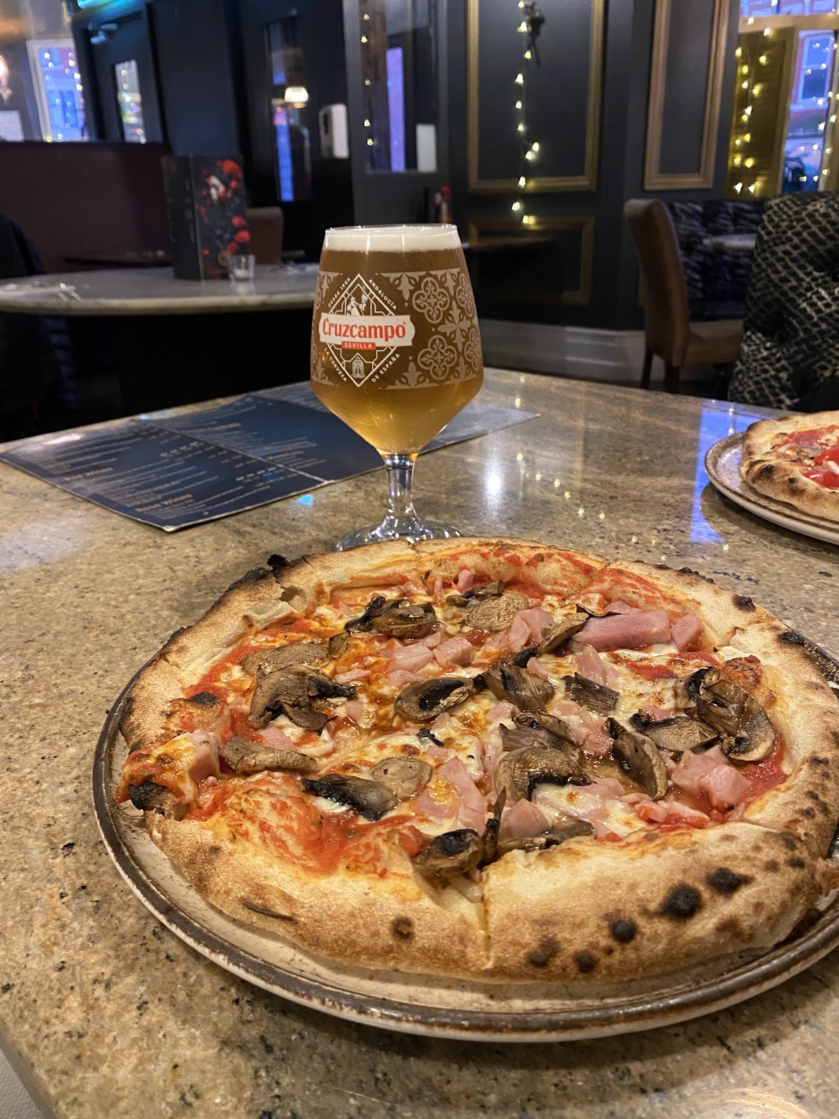 Ham and mushroom pizza with a cold beer on a marble table