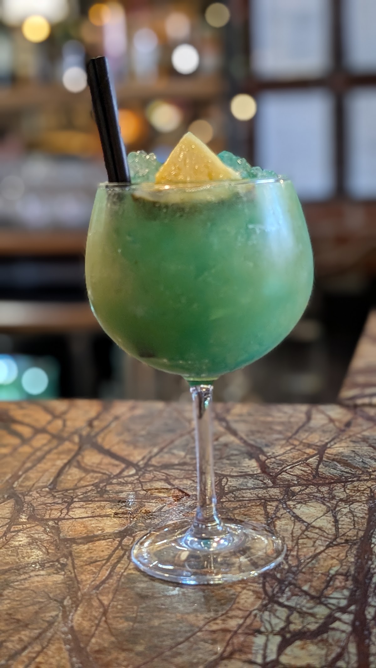 A green cocktail in a balloon glass on the marble bar
